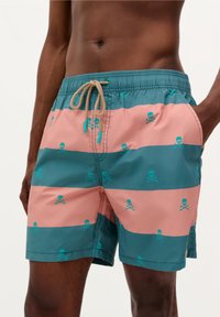 Shorts de bain avec des rayures horizontales rose et bleu canard, arborant un motif de tête de mort et os croisés. Matériau léger et cordon de serrage ajustable.