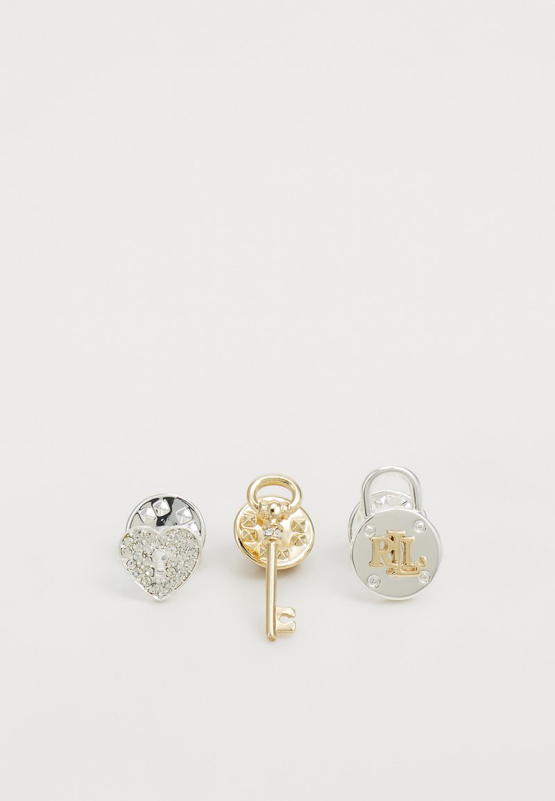 Tres accesorios de metal: a la izquierda hay un candado en forma de corazón plateado con rhinestones, en el centro hay una llave dorada con una base circular y a la derecha hay un candado plateado con "RL".