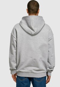 Sudadera con capucha gris de corte relajado, puños y dobladillo acanalados, y una textura suave. Presenta una gran capucha en la parte posterior.