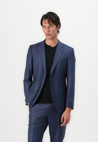 Blazer a cuadros azul marino hecho de tejido texturizado, con solapas de muesca, dos botones y bolsillos laterales, combinado con una camisa negra.
