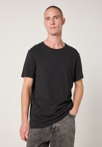 Črna majica s kratkimi rokavi iz mehke, teksturirane tkanine z okroglim izrezom, nošena z bledosivimi, spranimi kavbojkami.