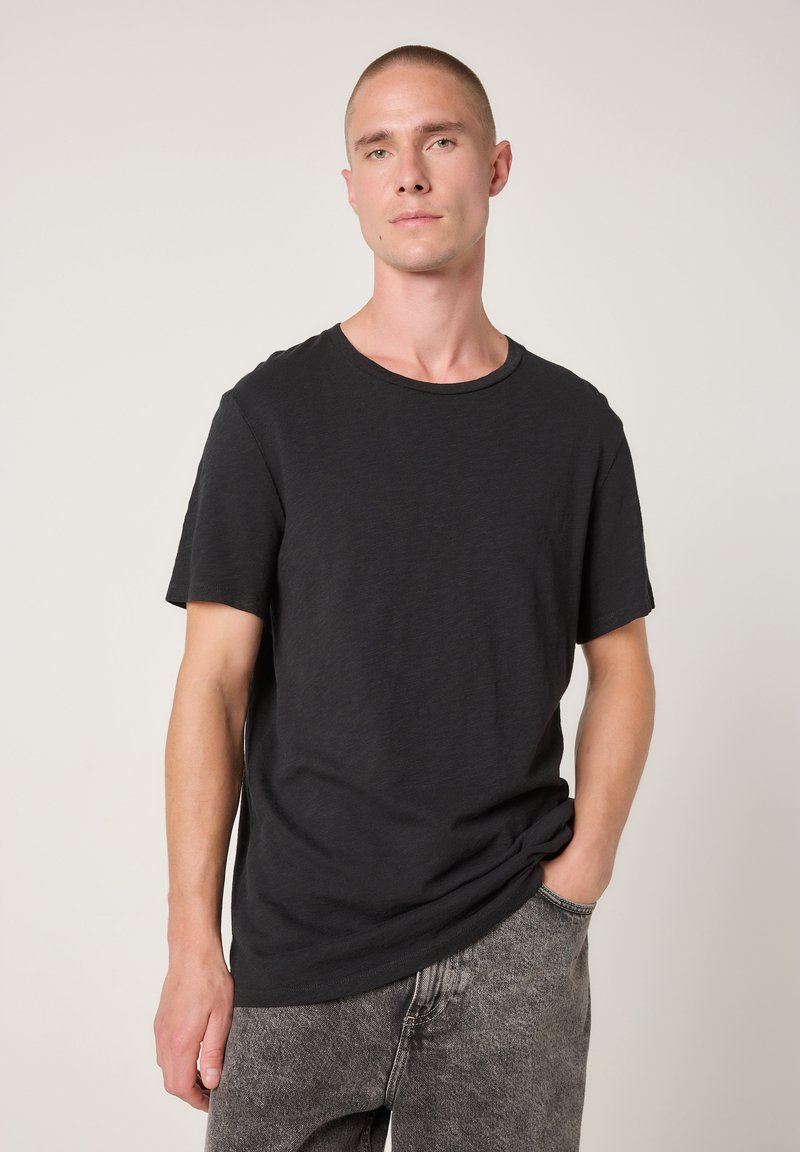 Črna majica s kratkimi rokavi iz mehke, teksturirane tkanine z okroglim izrezom, nošena z bledosivimi, spranimi kavbojkami.