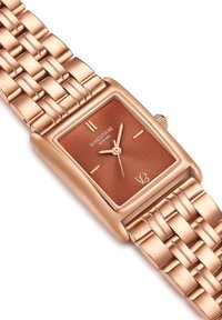 Reloj rectangular de oro rosa con un dial marrón texturizado, marcadores de hora plateados y una pulsera de metal trenzado. Destaca la corona de cuerda en el costado.