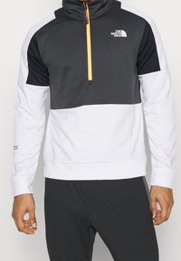 Pulóver de media cremallera para hombre en blanco y negro, con un diseño texturizado, acentos de color contrastantes y detalle del logo en el pecho y la manga.