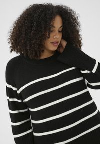 Black sweater with white horizontal stripes, ribbed neck and cuff details, soft texture; relaxed fit, round neckline.