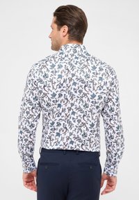 Camicia bianca a maniche lunghe con un intricato motivo floreale blu e marrone. Caratterizzata da una texture liscia e colletto standard, abbinata a pantaloni blu navy.