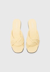 Gula slip-on sandaler med knutdesign, tillverkade av mjukt material, med en slät yta och en platt, svart sula.