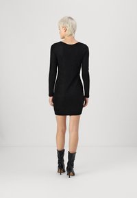 Vestido mini preto texturizado com mangas longas e costas em forma de scoop, combinado com botas altas pretas de salto. Design simples e ajustado.