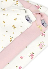 Τρία πουκάμισα στοιβαγμένα το ένα πάνω στο άλλο: ένα λευκό με κίτρινο ανθικό σχέδιο, ένα ροζ με διακοσμητικό φιόγκο, και ένα ακόμη λευκό με ροζ λουλούδια.