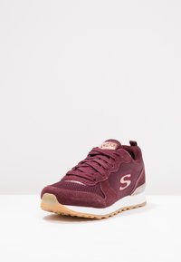 Burgundy athletic shoe with mesh and suede materials, lace-up design, textured upper, rubber sole, and a lightweight profile.