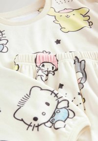 Weißes Fleece-Kleidungsstück mit verspielten Cartoonfiguren in schwarzer Kontur, verziert mit pastellfarbenen Akzenten und elastischem Taillenbund.