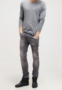 Maglietta grigia a maniche lunghe con scollatura rotonda, abbinata a jeans slim-fit grigi scoloriti e stivaletti neri alla caviglia. Design minimal e vestibilità casual.