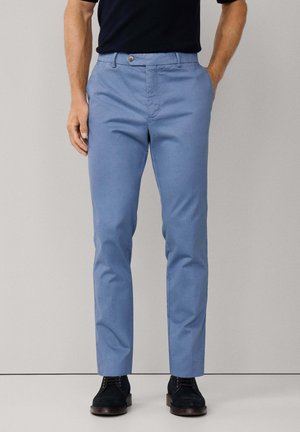 Pantalons en coton bleu clair avec une coupe droite, dotés d'une fermeture à bouton à l'avant et d'une texture lisse. Portés avec des chaussures foncées.