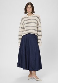 Pulover tricotat cu dungi crem și gri, asortat cu o fustă din denim bleumarin, completat cu pantofi slingback bej.