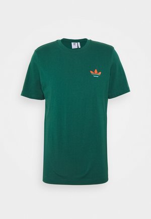 Ciemnozielona koszulka Adidas z krótkim rękawem, okrągłym dekoltem oraz małym pomarańczowo-białym logo Adidas Trefoil na lewej stronie klatki piersiowej.