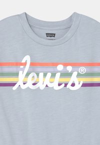 Jasnoniebieska koszulka Levi's z białym logo w formie pisma oraz poziomymi paskami w kolorach czerwonym, fioletowym, szarym, zielonym i żółtym na wysokości klatki piersiowej.