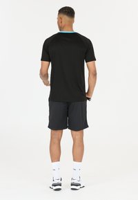 Svart tränings T-shirt med blå halsringning, tillsammans med svarta shorts. En texturerad tyg och lös passform som är lämplig för sport.
