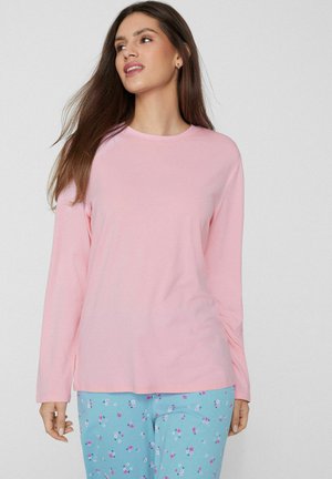 Chemise rose pâle à manches longues avec un col rond, associée à un pantalon bleu orné d'un motif floral rose et blanc. Texture de tissu douce.