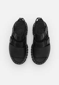 Svarta sandaler med en slät ovandel med två breda remmar och en texturerad fotbädd. Gummisulor med vita sömmar som detaljer.