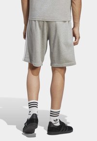 Shorts grii din bumbac, cu o talie elastică, având dungi laterale albe. Completate cu pantofi negri și ciorapi albi cu dungi negre.