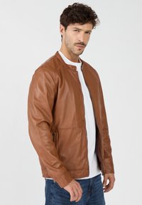 Braune Lederjacke mit glatter Textur, Druckknopfverschluss und Seitentaschen. Verfügt über ein figurbetontes Design und einen Stehkragen.