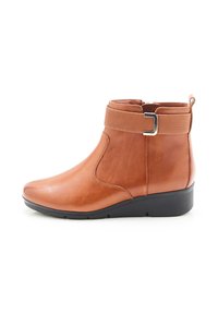 Botte de cheville en cuir brun avec une finition lisse, bout arrondi, fermeture éclair sur le côté et sangle élastique agrémentée d'une boucle en métal. Semelle en wedge basse.