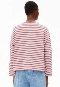 Gestreiftes Hemd in sanftem Rosa und Weiß, mit langen Ärmeln, Rundhalsausschnitt und einem dezenten Logo-Detail auf der Rückseite. Kombiniert mit blauer Jeans.
