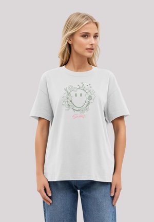 White cotton t-shirt with a round neckline and short sleeves. Features a green floral smiley design and pink "Smiley" text at the bottom.