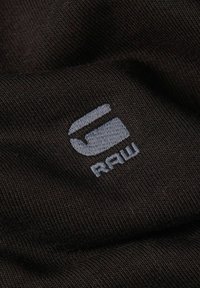 Tessuto nero testurizzato con un logo ricamato grigio, composto da una "S" stilizzata e la parola "raw" in lettere minuscole.