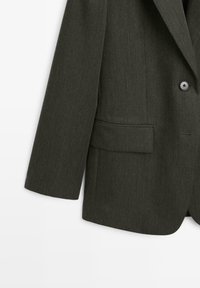 Blazer verde scuro con tessuto testurizzato, chiusura a singolo bottone e vestibilità dritta. Caratterizzato da una tasca frontale e rever a punta.