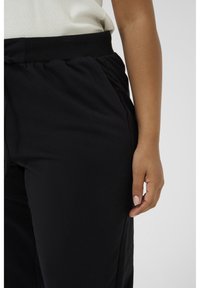 I pantaloni jogger neri presentano un girovita con cordino, tasche laterali e una texture morbida e liscia con una vestibilità slim lungo la gamba.