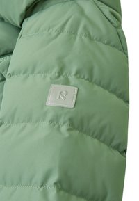 Jachetă verde cu umplutură, cu o textură matlasată, având un mic patch rectangular de culoare verde deschis pe mânecă. Material ușor.