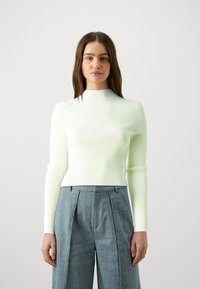 Geribbelde gebreide langemouwen top in lichtgroen met een hoge hals, gecombineerd met plooibare lichtblauwe wijde broek. Gladde textuur.