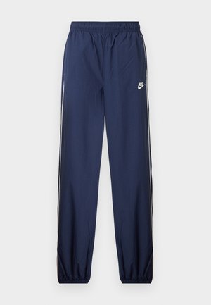 Námornícke modré tepláky Nike s elastickým pásom, bielymi bočnými prúžkami a malým logom na ľavom stehnu. Textúrovaná látka, zúžené manžety.