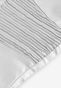 Texturerad vit tyg med vertikala veck på ena sidan och slät, enfärgad material på den andra, med en stygnkant som detalj.