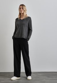Grå stickad tröja med V-hals och ribbad textur, kombinerad med svarta vida byxor och vita sneakers. Enkel, avslappnad outfit.
