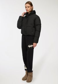 Czarna puchowa kurtka z kapturem, o pudełkowym kroju i pikowanym wzorze. W połączeniu z czarnymi dresami i brązowymi trzewikami z baranka.