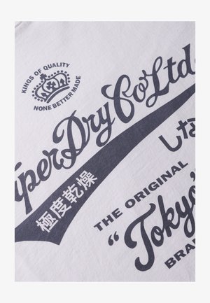Camiseta de algodón blanca con un diseño gráfico en texto azul oscuro, que incluye "SuperDry Co Ltd" y un logo de corona, con caracteres japoneses incluidos.