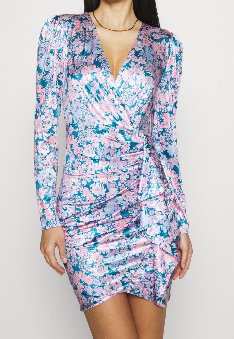 Femme portant une mini-robe brillante à manches longues, froncée, avec un motif floral rose et bleu et un décolleté en V profond.