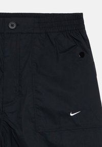 Shorts de sport noirs en tissu léger, dotés d'une taille élastique, d'une fermeture à bouton et d'un logo Nike blanc à l'ourlet.