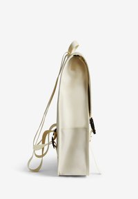 Un sac à dos de couleur crème avec une texture lisse, doté d'une fermeture à cordon, de bretelles ajustables et d'une poche avant. Forme rectangulaire.