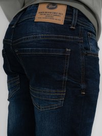 Tmavě modré džíny z denimu mají koženou nášivku s označením "Petrol." Denim má hladkou strukturu s viditelnými švy.