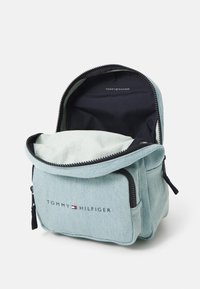 Šviesiai melsvas džinsinis kuprinės su juodu užtrauktuku, turinti vieną pagrindinę compartmentą ir Tommy Hilfiger logotipą priekyje.
