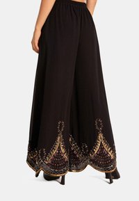Zwarte wijdelopige broek met een elastische tailleband. Kenmerkt zich door ingewikkelde gouden en gekleurde borduursels langs de zoom, met een geometrisch ontwerp.