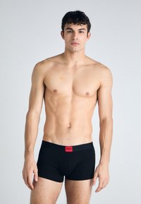 Schwarze Boxer Shorts mit einem roten HUGO-Bund, aus weichem Stoff, mit eng anliegendem Schnitt und einem schlichten, klaren Design.