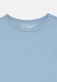 Ανοιχτό μπλε, κοντομάνικο μπλουζάκι με στρογγυλή λαιμόκοψη και απαλή υφή. Η ετικέτα γράφει «FRIBOO» και μέγεθος 98/104 εκ.