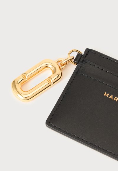Porte-cartes en cuir noir avec bords cousus, muni d'une fermeture métallique dorée fixée à un coin.