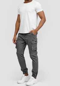 Grå cargobyxor med sidfickor, avsmalnande mudd och en avslappnad passform, kombinerade med en vit T-shirt med rund hals och vita sneakers.
