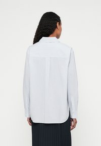 Light blue button-up shirt with thin vertical stripes, long sleeves, and a back yoke; made of woven fabric with a smooth texture.