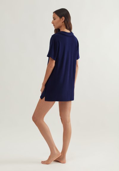 Παντελόνι πόλο σε σκούρο μπλε χρώμα, με κοντά μανίκια, κατασκευασμένο από υφή υφασμάτων. Διαθέτει γιακά και σκισίματα στα πλάγια για επιπλέον ευκινησία.